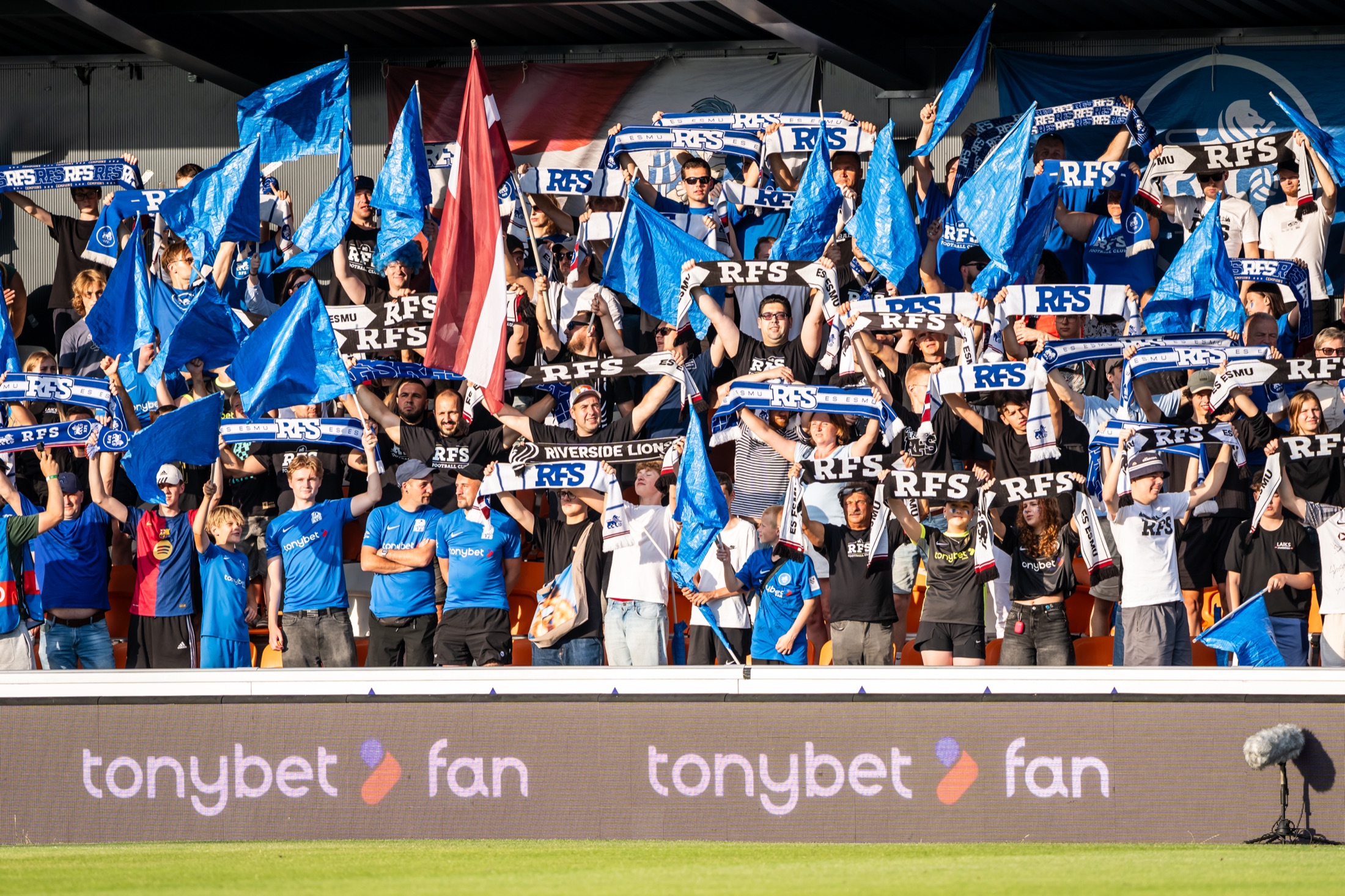 FC RFS līdzjutēji tribīnēs ar zilajiem karogiem un šallēm
